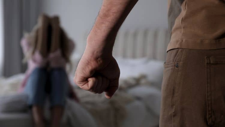 Mann ballt Faust, Frau sitzt mit Armen vor Gesicht auf Bett