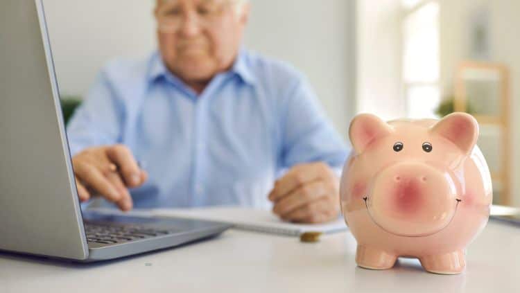 Rentner am PC und Sparschwein auf Tisch